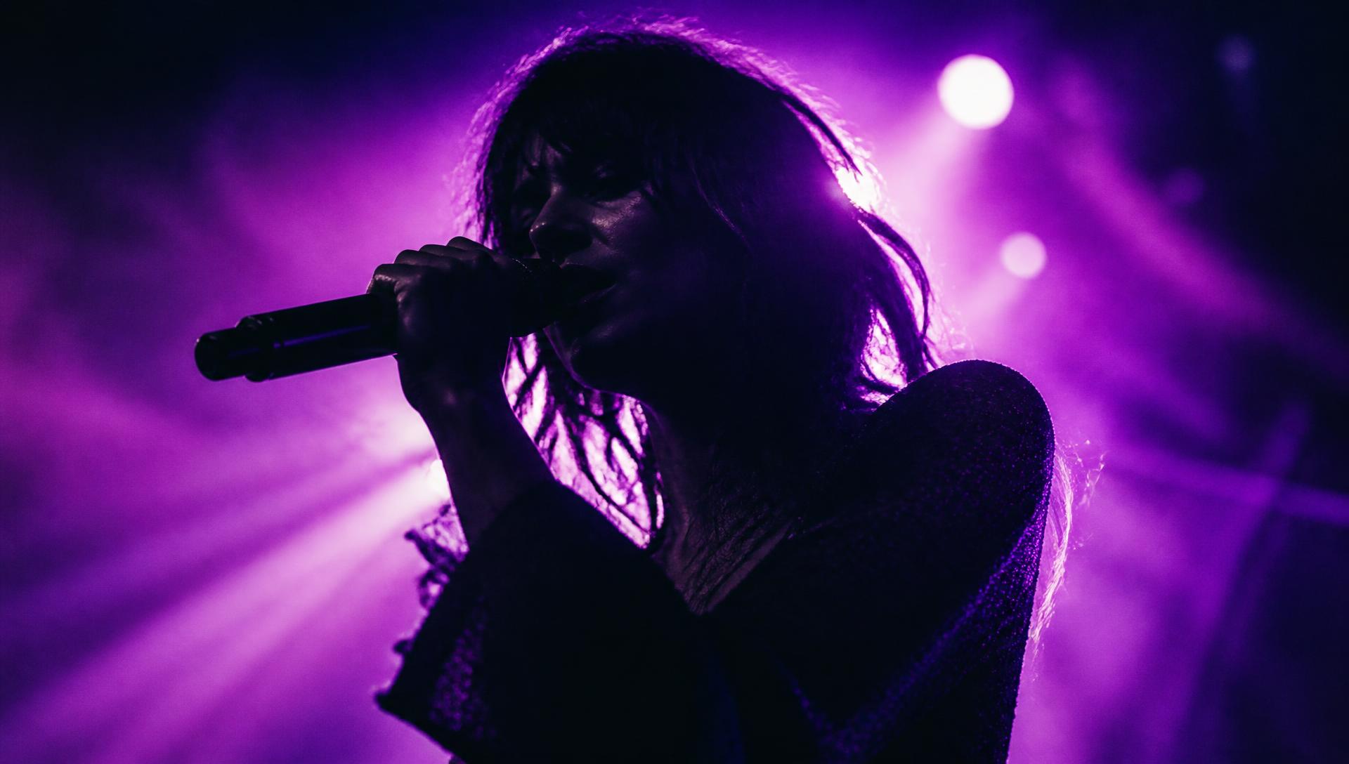 Performer singing on stage in dense purple stage light